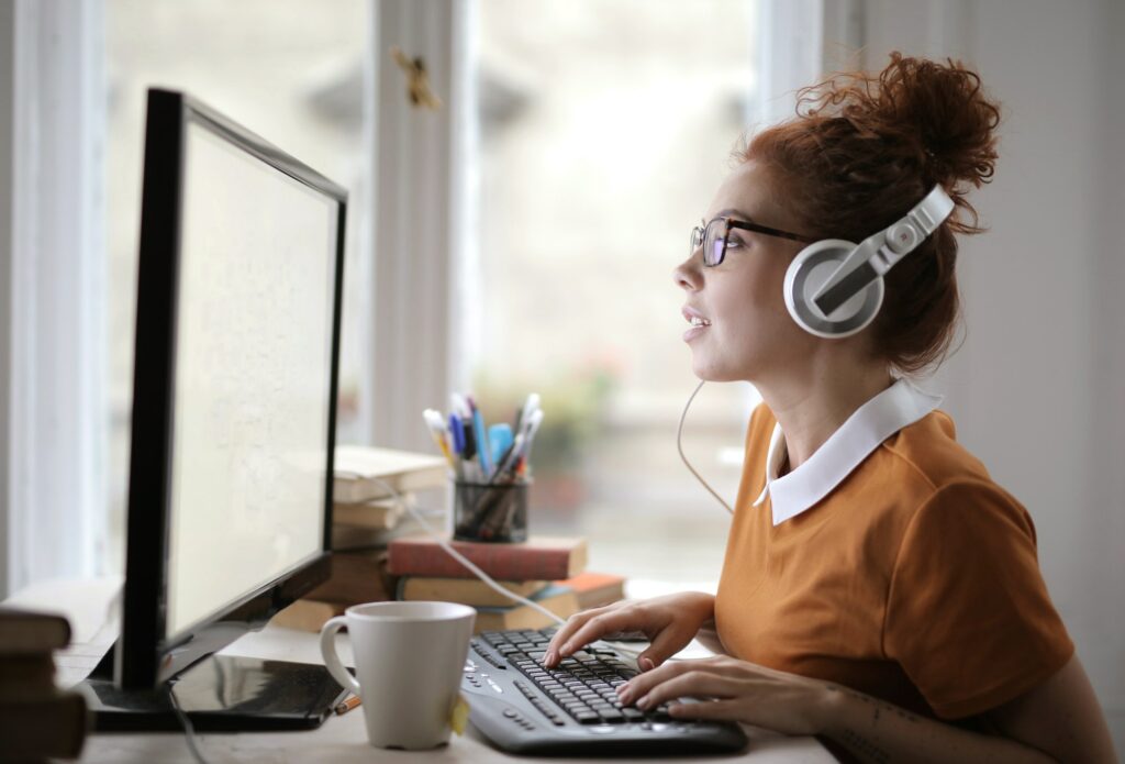 Young woman with headphones and glasses working on the computer under the lights in a house